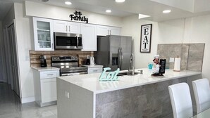 A modern kitchen with white cabinetry, stainless steel appliances, and a central island with seating.