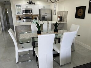 Une cuisine moderne avec des meubles blancs, des appareils en acier inoxydable et une table à manger en verre, assortie de chaises blanches.