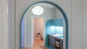 A narrow hallway leading to a kitchen with a modern design, featuring a blue accent wall and a white ceiling light. - ReLiving – Your Group’s Perfect Getaway (Luzern)