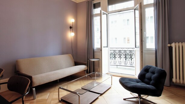 A modern living room with a sofa, a chair, a glass coffee table, and a balcony with a view. - ReLiving – Your Group’s Perfect Getaway (Luzern)