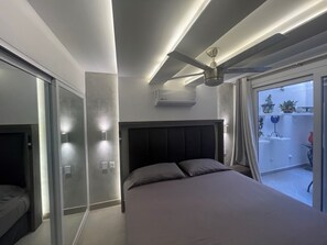 A modern bedroom with a bed, a ceiling fan, and a view of the outside balcony.