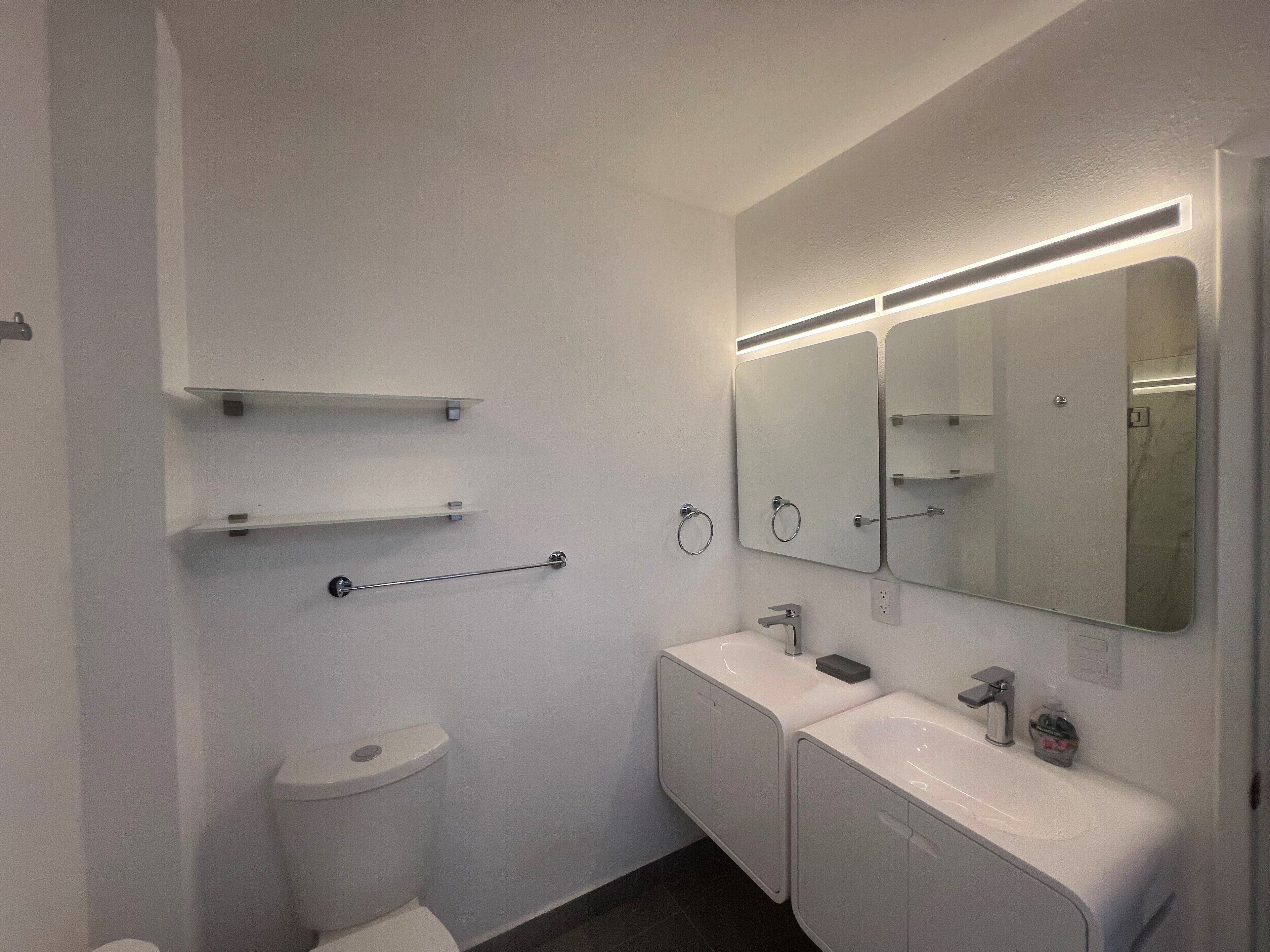 Une salle de bain moderne équipée d’un WC, de deux lavabos, d’un miroir et d’un porte-serviettes.