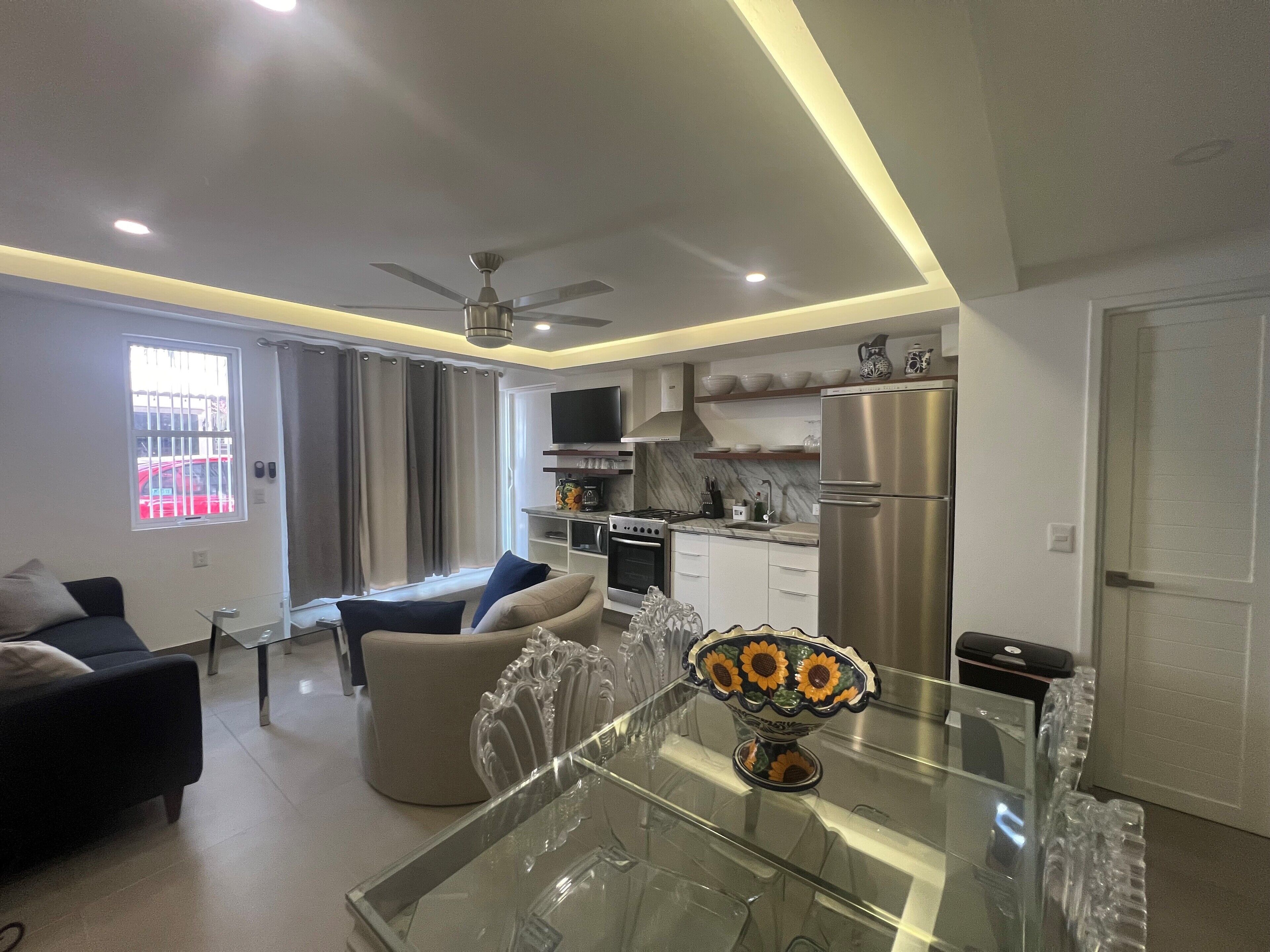 A modern living room with a glass dining table, a sofa, and a TV.