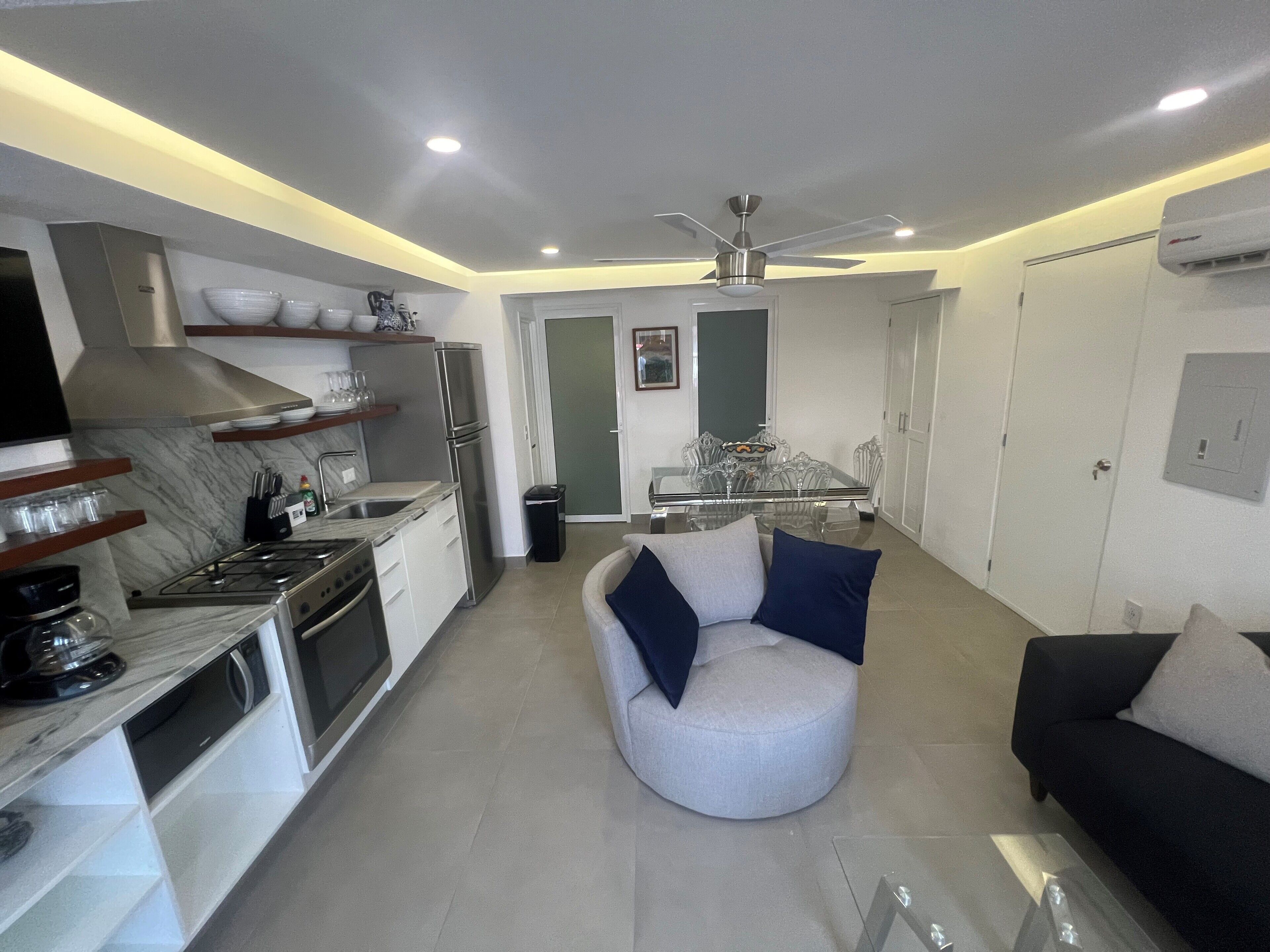 A modern kitchen with a dining area, a ceiling fan, and a sofa with cushions.