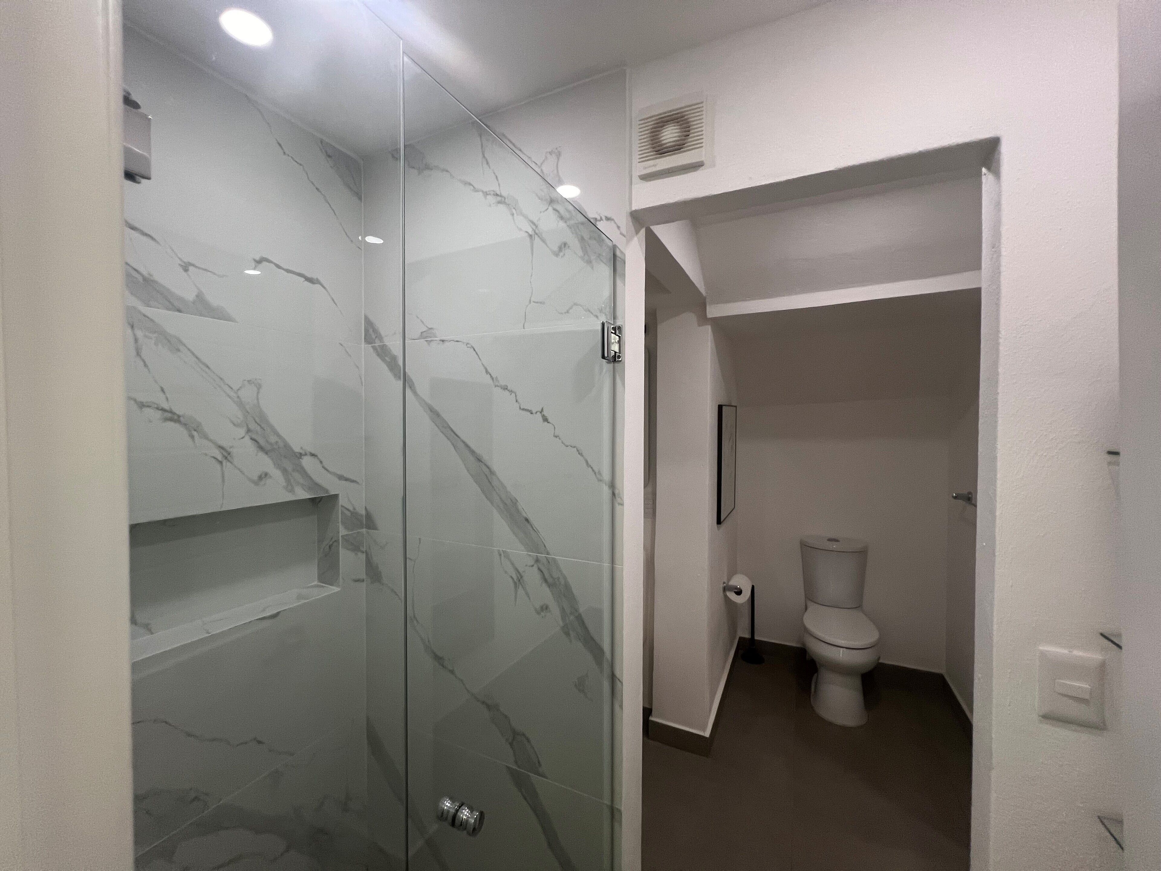 Un baño moderno con ducha acristalada, inodoro y pared de mármol.