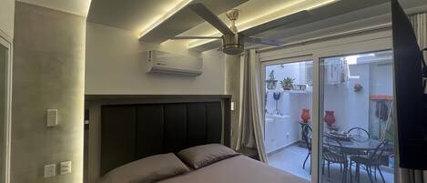 A bedroom with a bed, a ceiling fan, an air conditioning unit, and a view of the outside balcony.