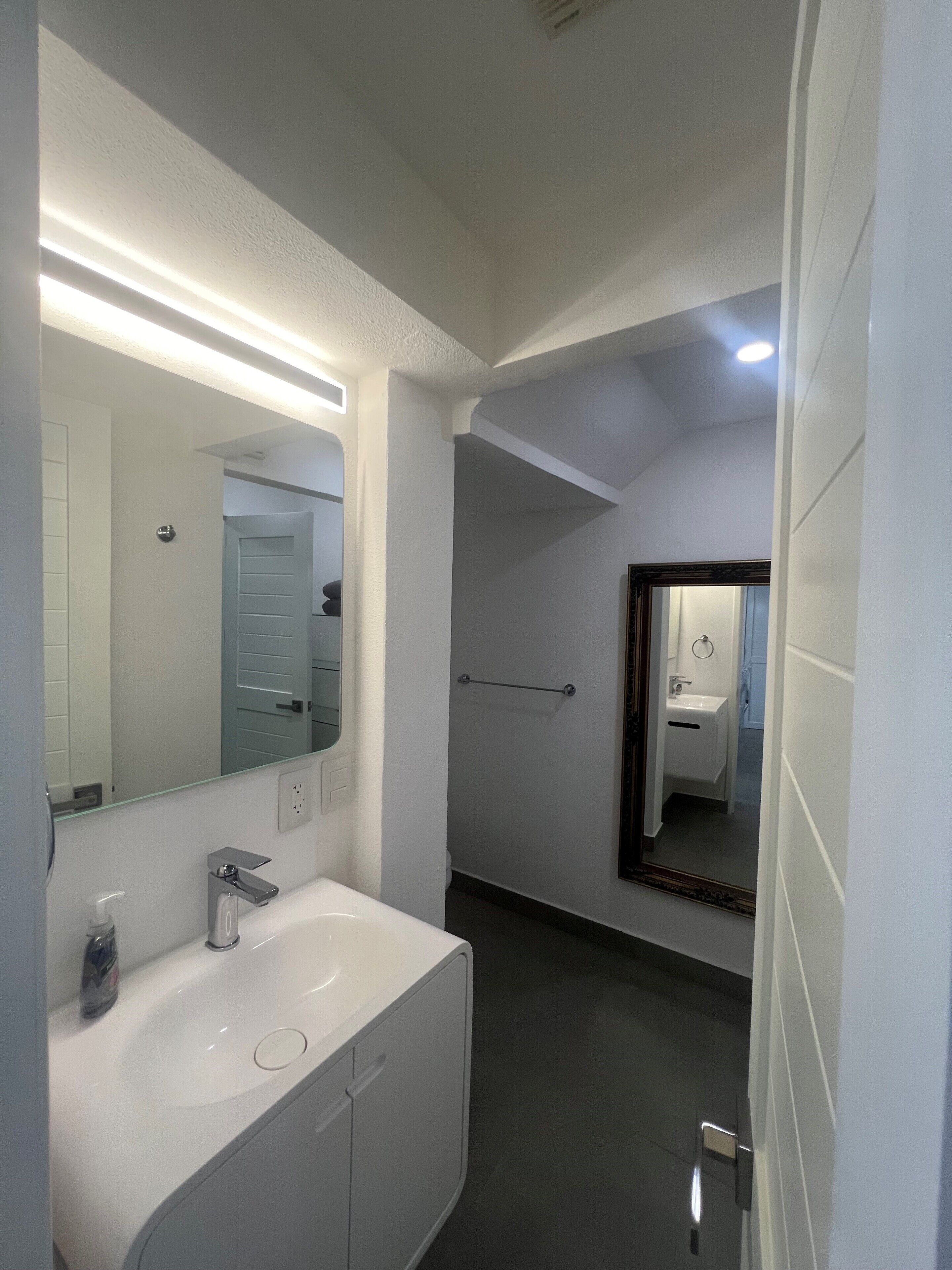 Une salle de bain moderne avec un grand miroir, un lavabo blanc et un espace douche.