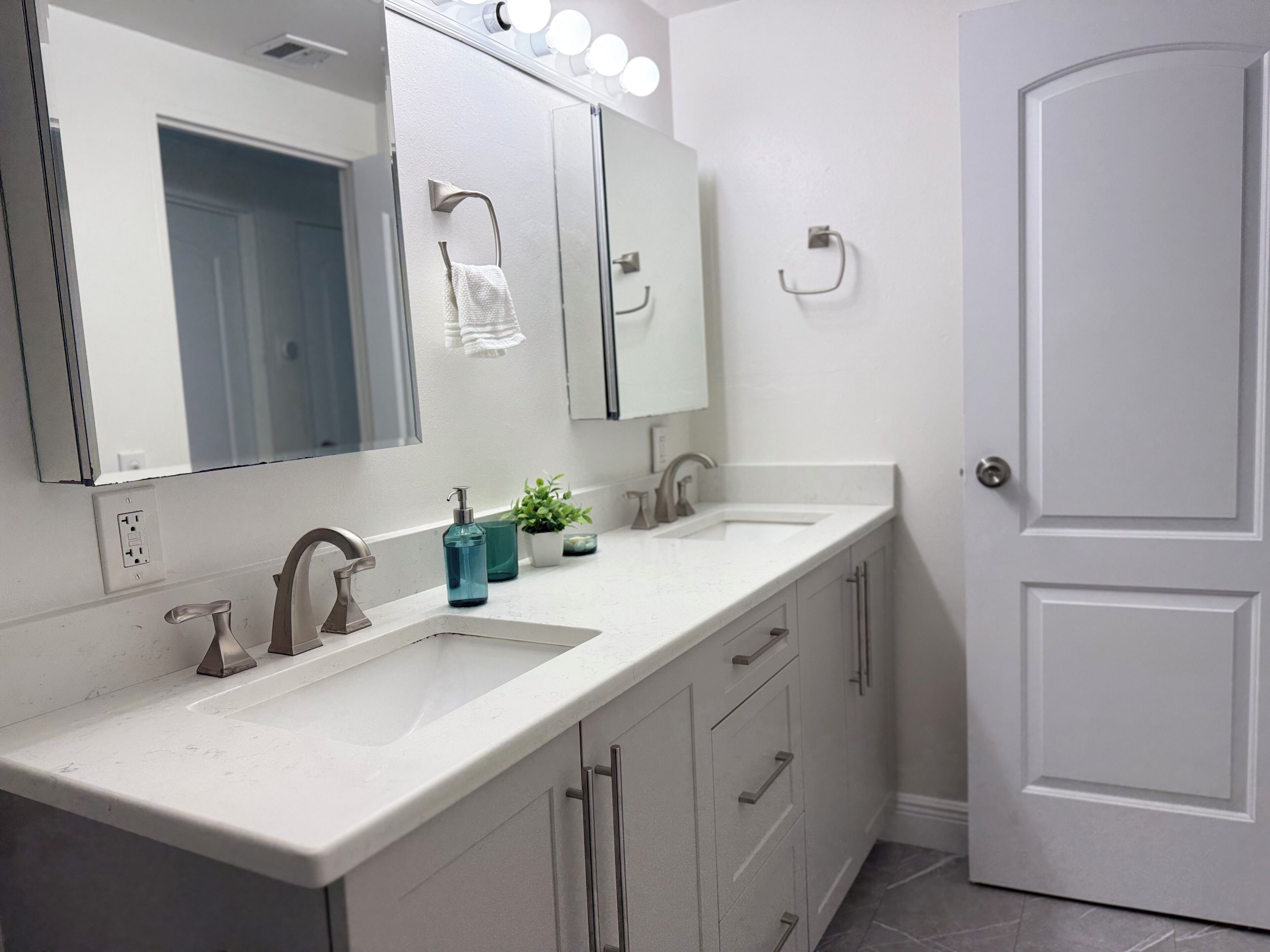A modern bathroom with a white vanity, two sinks, a large mirror, and a door.