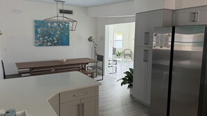 Eine moderne Küche mit einer zentralen Kochinsel, einem Essbereich mit Tisch und Stühlen sowie einem Kühlschrank.