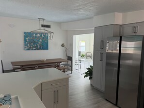 A modern kitchen with a central island, a dining area with a table and chairs, and a refrigerator.