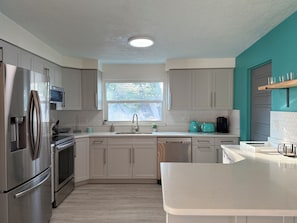 A modern kitchen with stainless steel appliances, a window with a view of greenery, and teal accent walls.
