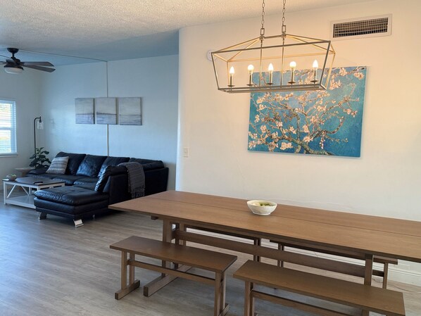 A modern living room with a wooden dining table, benches, a black leather sofa, and a ceiling fan. - Beautiful 3-bedroom house 1 mile from Indian Rocks Beach (Largo)