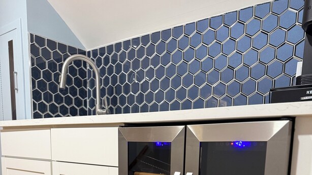 Una cocina moderna con refrigerador de acero inoxidable, armarios blancos y un salpicadero de azulejos hexagonales azules.