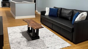 Una sala de estar moderna con un sofá de cuero negro, una mesa de centro de madera y una alfombra estampada.