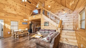 Interior de una cabaña de madera con comedor, sofá y escalera.