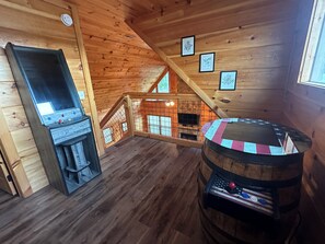 Cozy cabin interior with a high ceiling and wooden walls, featuring a rustic entertainment area with a wooden table and jukebox.