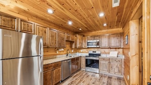Una cocina de estilo rústico con muebles de madera, un refrigerador de acero inoxidable, un lavavajillas, un microondas y un horno.
