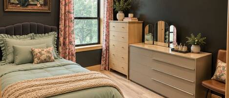 A bedroom with a bed, dresser, vanity, and a ceiling fan.