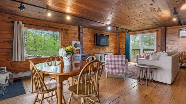 Interior de una cabaña de madera con una mesa de comedor, sillas, un sofá y un televisor.