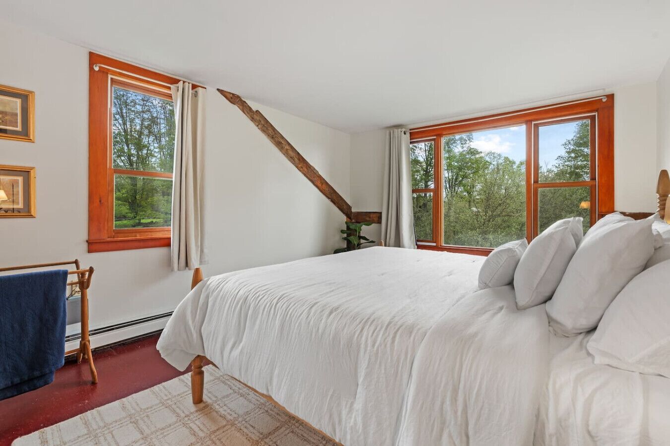 A bedroom with a large bed, two windows, a wooden beam, a radiator, and a towel rack.