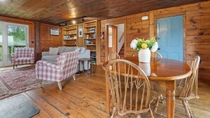 Un interior de cabaña acogedor con una mesa de comedor de madera, sillas a cuadros, un sofá y una estantería.