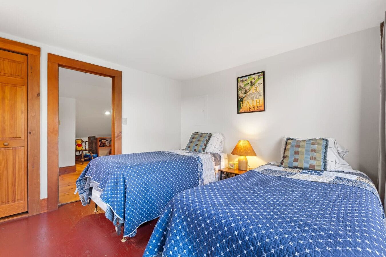 A room with two beds, a wooden door, a mirror, and a wall-mounted lamp.