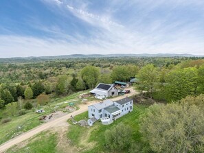 A large, two-story house with a solar panel on the roof, surrounded by a lush green landscape and a clear sky.