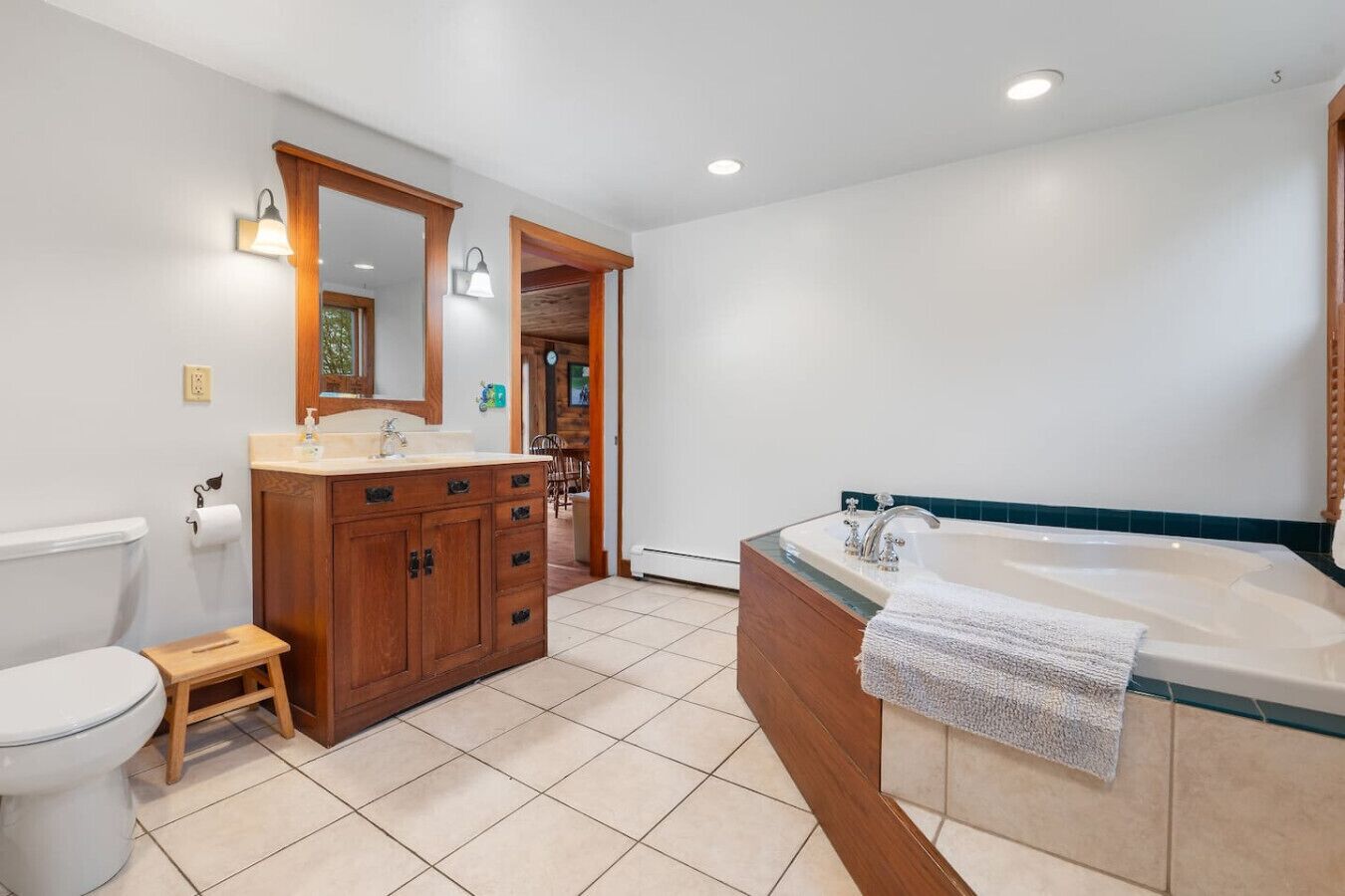 Une salle de bain comprenant des toilettes, un meuble-lavabo en bois avec un évier, une grande baignoire et un miroir.