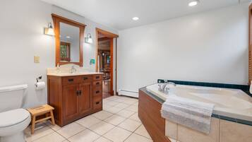 Une salle de bain comprenant des toilettes, un meuble-lavabo en bois avec un évier, une grande baignoire et un miroir.