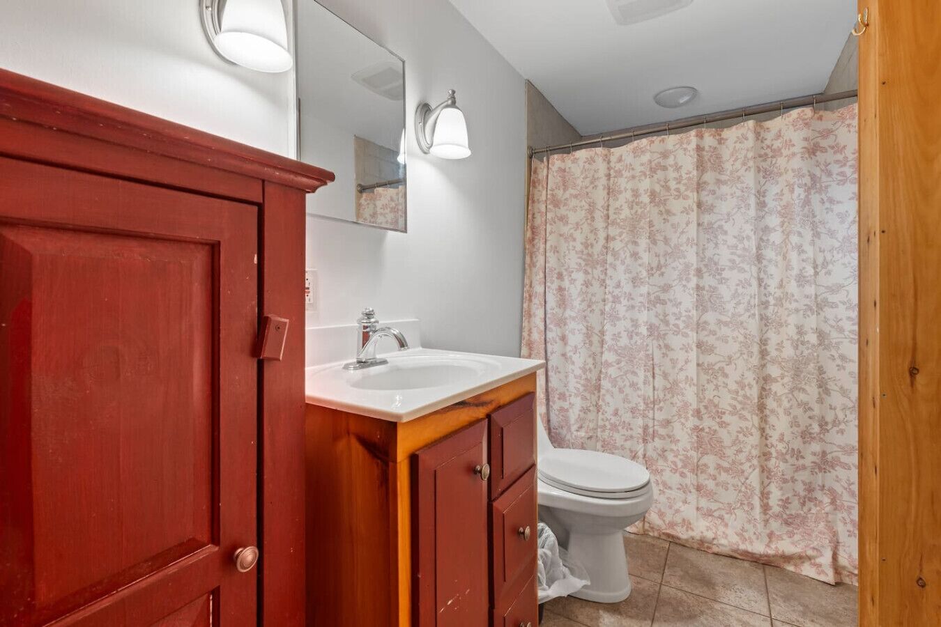 A bathroom with a wooden vanity, a white sink, a mirror, a toilet, and a shower curtain.