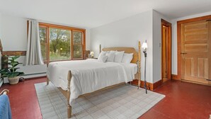 Un dormitorio con una cama grande, una ventana con cortinas, una planta en maceta y una puerta de madera.