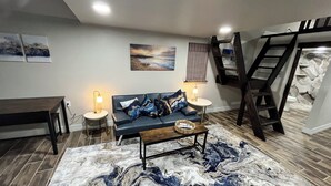 Una sala moderna con un tapete estampado tipo mármol, un sofá de cuero oscuro con cojines estampados, una mesa de centro de madera y dos lámparas fijadas a la pared.