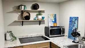 Una cocina con armarios de madera, encimera de granito, estufa, microondas y estantes con adornos.