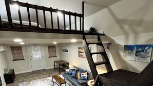 Un espacio tipo loft con una escalera de madera, un sofá, una mesa de centro y un tapete grande de diseño abstracto.