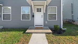 A two-story house with a gray siding exterior, a white front door, and a small porch with a welcome mat. - Townhouse near WKU & Mammoth Cave (Bowling Green)