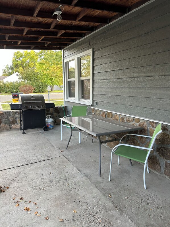An outdoor patio with a grill, table, and chairs.