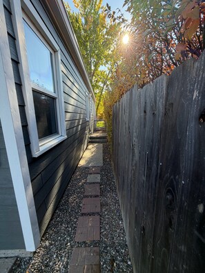 A narrow pathway leading to a house with a window and a wooden fence.