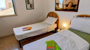Une petite pièce simple, avec deux lits simples, une petite table, une table de chevet et une fenêtre donnant sur des immeubles.