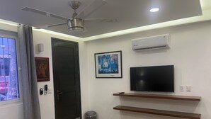 A modern hotel room with a bed, a ceiling fan, a mounted TV, and a small trash bin.