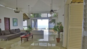 Un salon spacieux, doté d’un grand canapé, d’une table basse et offrant une vue sur l’océan grâce à de grandes fenêtres.