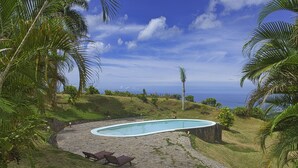 Une piscine à bordures courbes, entourée d’une terrasse en pierre et agrémentée de deux chaises longues en bois.