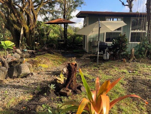 Un jardín con una estructura de madera rústica, una mesa de metal y un paraguas grande.