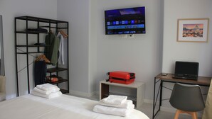 Habitación de hotel con cama, un escritorio con una computadora portátil, un televisor montado en la pared, un armario y un cuadro enmarcado en la pared.