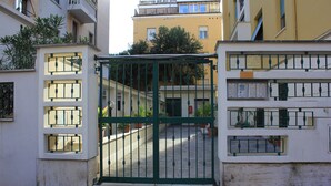 Una entrada con portón metálico, una escalera que lleva a un edificio y plantas en macetas.