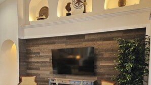 Ein Wohnzimmer mit großem Flachbildfernseher, Holzwandverkleidung und einem blauen Sofa.