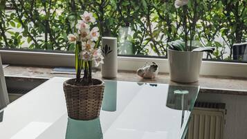 Una mesa con cubierta de vidrio y una cesta de mimbre que contiene orquídeas blancas, una taza de cerámica y una pequeña figura de pájaro.