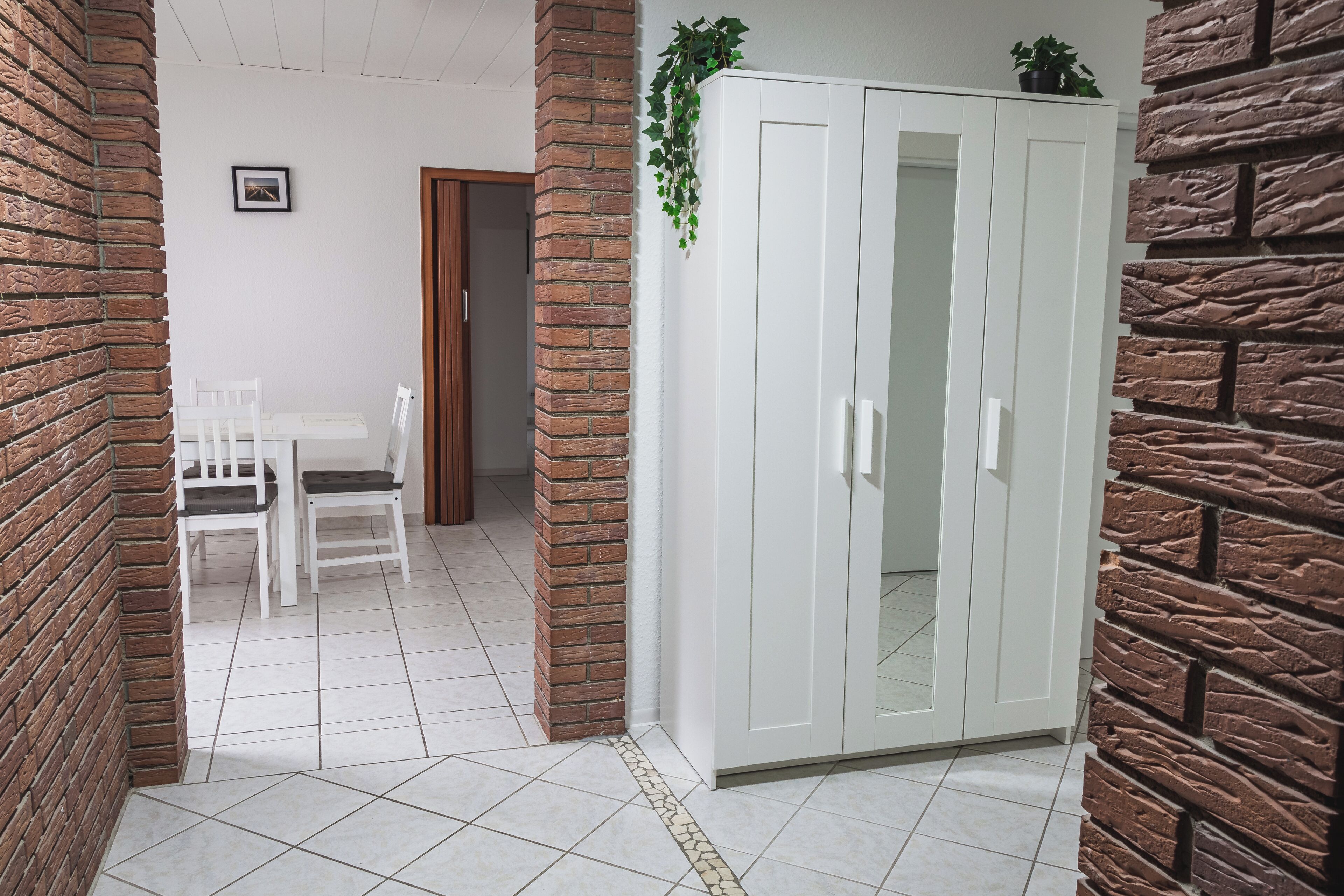 Ein Zimmer mit einem weißen Kleiderschrank, einem Esstisch mit Stühlen und einer Ziegelwand.