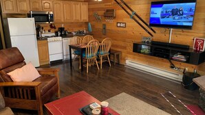 A cozy living room with a red table, a leather couch, and a TV mounted on a wooden wall. - Cozy Condo, 3 beds, 2 baths, kitchen, near RMNP, Hiking, Golf, Skiing and more! (Granby)