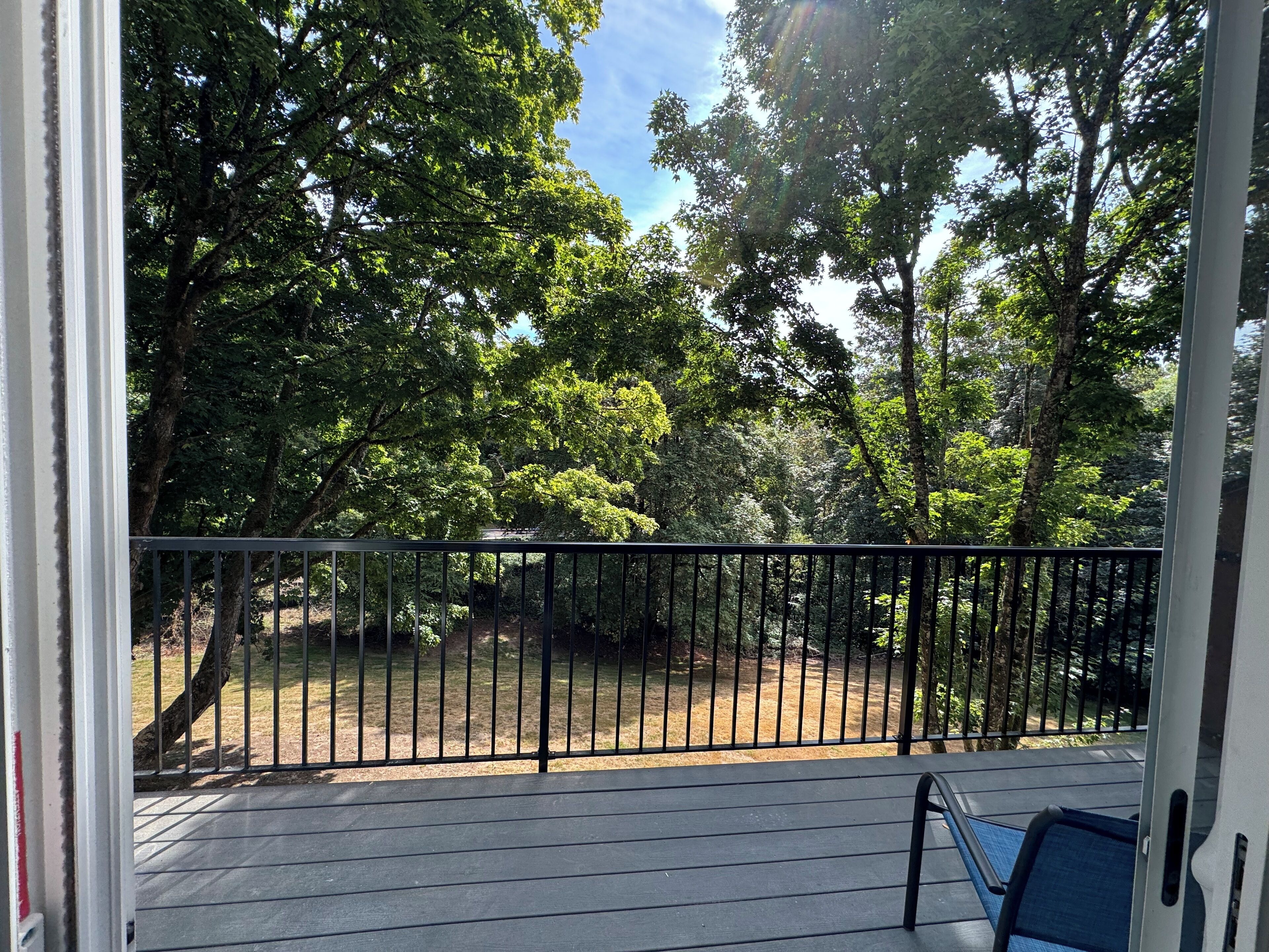 A balcony with a metal railing, a blue chair, and a view of a wooded area.