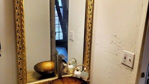 Un bany amb un mirall gran i ornamentat, un tocador de fusta, un lavabo i un lluminari sobre el mirall.